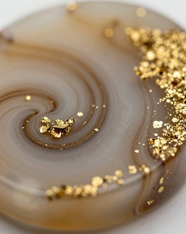 A detail-oriented macro shot of an intricate resin piece with shimmering gold flakes and soft #8C6B5E swirls. Polished, high-gloss finish under soft studio lighting.