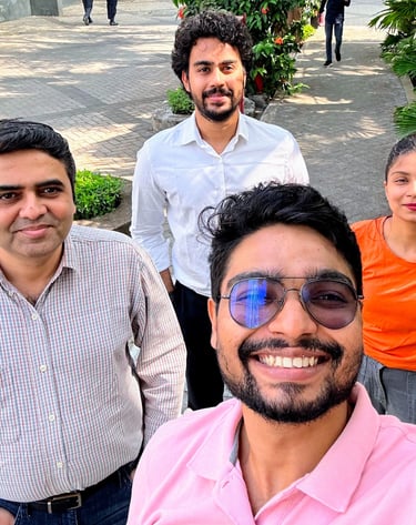 A diverse group of four smiling office colleagues taking an outdoor selfie at their workplace courtyard.