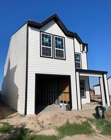 A modern two-story house under construction with white horizontal siding and black window frames.