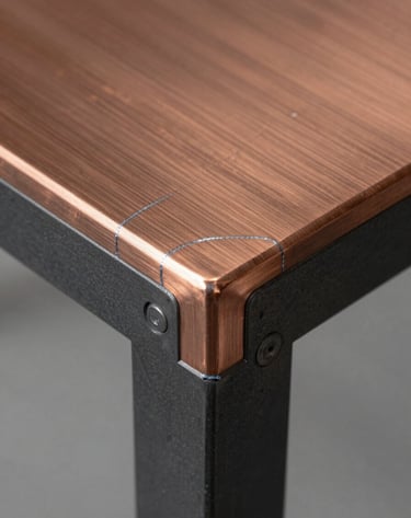 Macro photography of a furniture joint where brushed copper meets dark charcoal steel. The image showcases the technical precision and clean welding lines that define Rawline's craftsmanship. Soft, professional studio lighting.