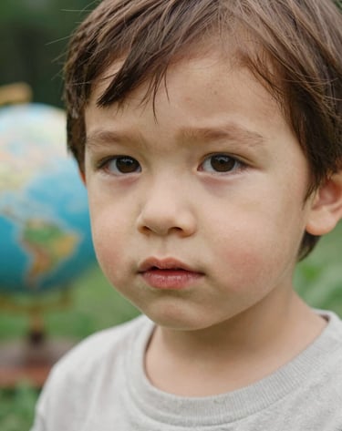 Close-up candid portrait of a child in a Western / Global garden, soft natural lighting, authentic expression, warm almond and soft sand color palette, shallow depth of field.