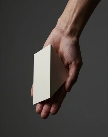 Close-up artistic photography of a human hand and arm positioned to create abstract geometric shapes. The lighting is moody and focused, using off-white highlights against a dark charcoal grey environment. Minimalist and refined composition in a North American / US studio.