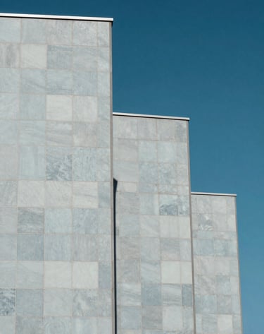 Detailed exterior view of a modern building facade featuring Light grey-blue porcelain tiles. Sharp architectural angles against a clear blue sky. Conceptual and artistic perspective, European / Portuguese architecture.