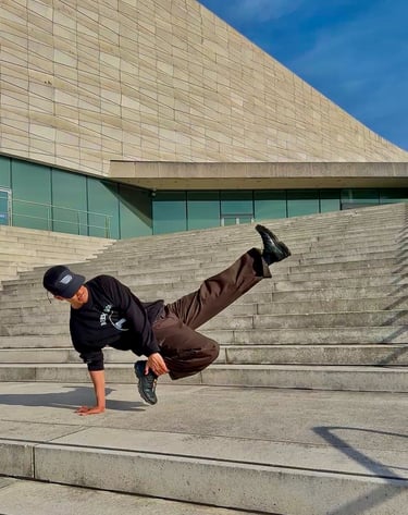 YoYo performing a breakdance move in front of concrete building.