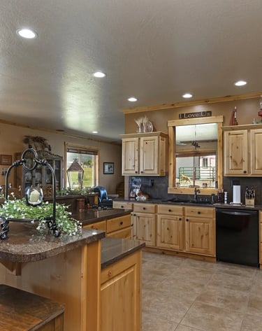 a kitchen with a large island and a black refrigerator, custom wood cabinets, and granite tops