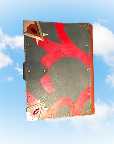 Handcrafted leather grimoire with red inlay, brass corners, and ruby gems floating against a blue sky.