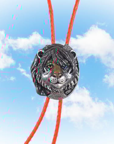 A silver lion head bolo tie with green and blue eyes on a red braided cord against a blue sky.