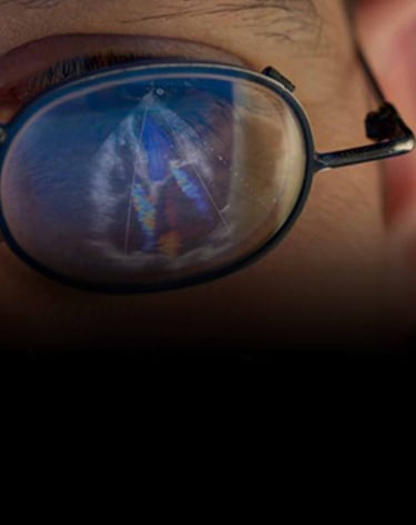 A person wearing round eyeglasses reflecting a medical echocardiogram heart ultrasound scan on the lens.