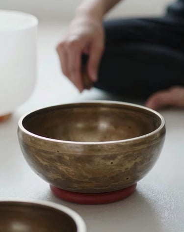 Close-up artistic shot of a metal singing bowl used in music therapy. The hands of a practitioner are blurred in the background. Minimalist studio setting in North America. Soft, natural lighting, deep blacks and bright whites.