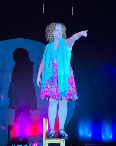ein lockiges Mädchen auf einem Stuhl stehend im Spotlight auf der Bühne