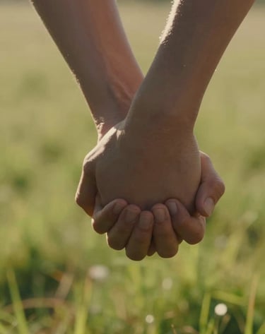 A close-up, cinematic detail shot of two hands holding tightly against a backdrop of sun-drenched meadow. The lighting is warm and inviting, emphasizing a genuine human connection.
