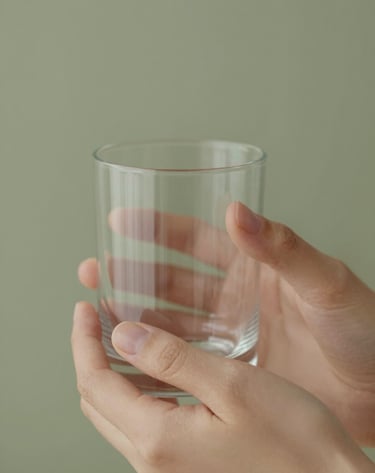 Macro shot of delicate hands holding a glass of water or a luxury beauty product, soft focus, emphasizing texture and elegance. Palette includes #6B705C olive tones in the background.