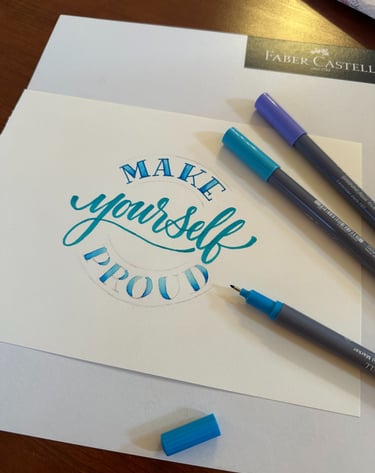 Hand-lettered blue calligraphy saying Make Yourself Proud with Faber-Castell brush markers.