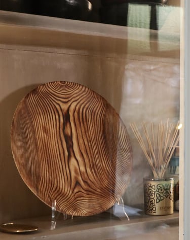 Handcrafted decorative wooden plate with natural grain on a display shelf next to a reed diffuser.