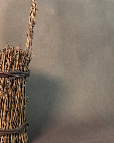 Close-up of a rustic handcrafted bamboo bud vase featuring bundled dried twigs and a natural fiber handle.