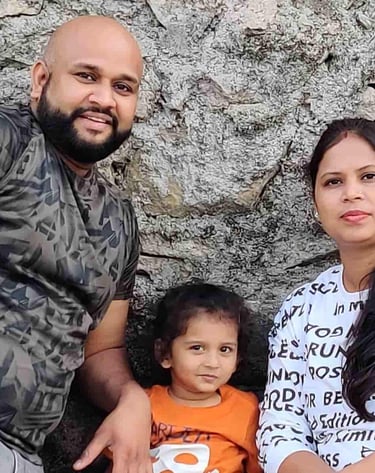 A happy family with a father, mother, and young child posing together in front of a stone wall.