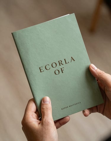 A detail shot of a hand holding a sage green program booklet. Soft focus background featuring the warm taupe textures of the venue. Elegant, professional photography style.