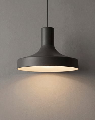 A minimalist architectural lighting fixture with a matte charcoal finish hanging against a greige textured wall, warm ambient glow, South American contemporary interior style.