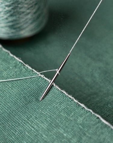 Macro photography of silver thread being woven into a piece of soft green linen fabric, sharp focus on the needle, magical shimmering particles in the air, professional studio lighting.