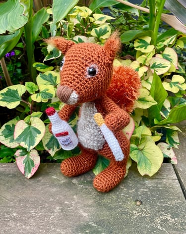 a crochet of a stuffed squirrel holding a bottle of vodka and a cigarette 