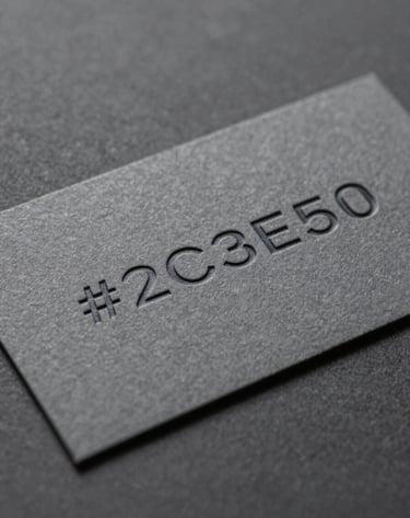 Macro photography of a premium business card featuring deep-etched typography on heavy-weight #2C3E50 paper stock. The lighting highlights the tactile texture of the paper and the sharp edges of the minimalist print design, showcasing forward-thinking creativity.