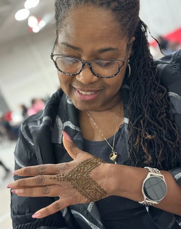 Black woman with glasses looks at the henna on her hand and smiles