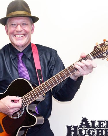 aled hughs in a hat and tie dyes playing guitar