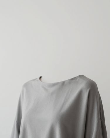 A minimalist portrait with an emphasis on negative space. The subject is draped in a refined fabric of #6B625E against a background of #AEAEA7. High-quality lighting creates an elegant, professional mood.