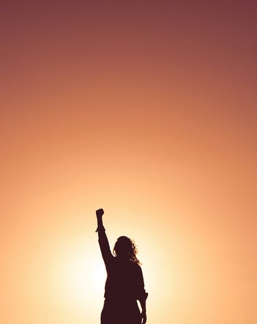 a person standing in front of a sunset with their hand raised