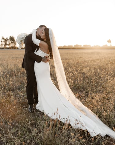a bride and groom kissing in a field at sunset