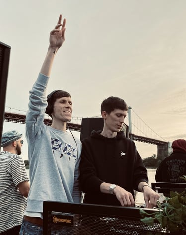 Two dj men standing in front of a large screen