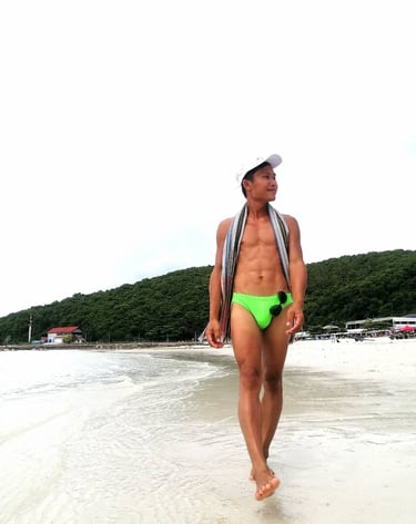 Man walking along Pattaya Beach wearing green swimming trunks.