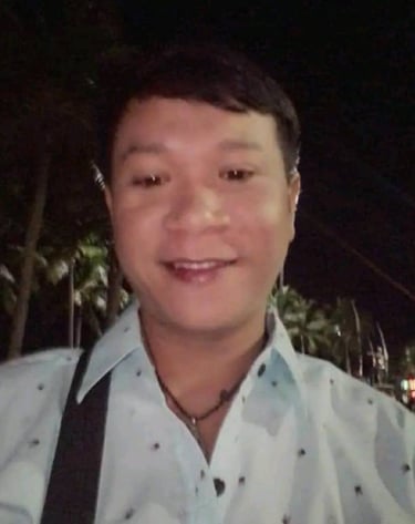 Male therapist smiling at night in Pattaya, Thailand, wearing a light shirt and shoulder bag.