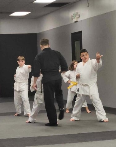 Young students in white uniforms practice karate moves during a martial arts class with a black-clad instructor.