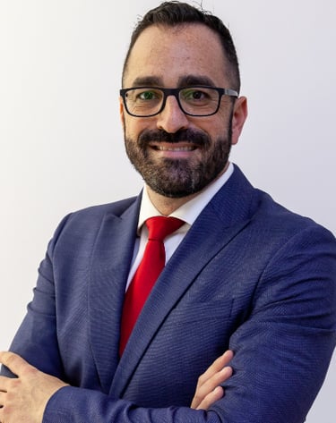 Professional headshot of a smiling businessman in a blue suit and red tie wearing glasses.