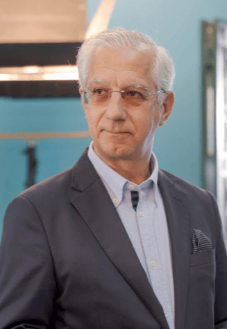 Professional senior man wearing a navy blazer and light blue shirt in a studio setting.