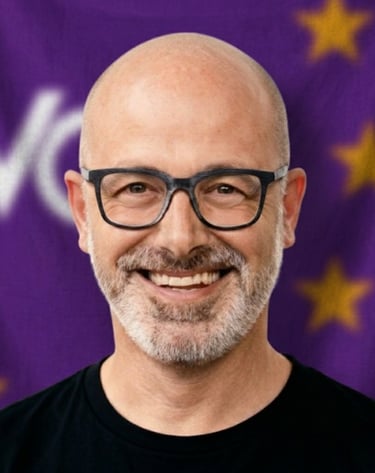 A smiling bald man with glasses and a beard in front of a purple Volt Europa flag.