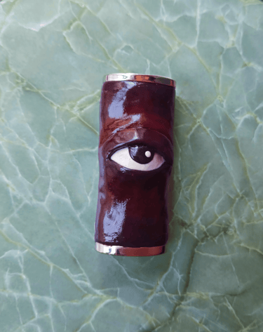 Shiny maroon hand-made lighter case with a sculpted 3D eye in the middle. 