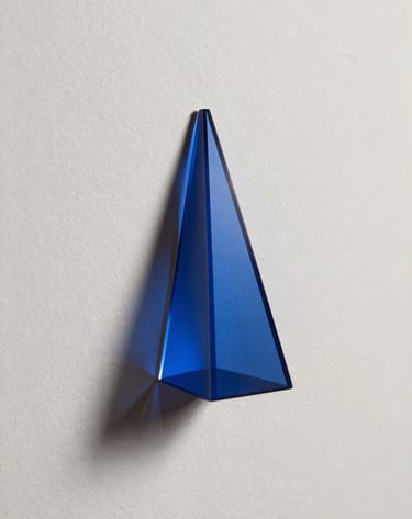 Clean, minimalist photography of a glass prism catching a beam of light, casting a spectrum of Deep Prussian Blue shadows onto a Soft Off-White textured background. Intellectual and architectural in style.