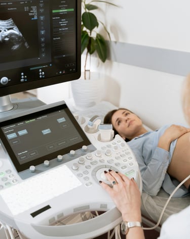 A pregnant patient receiving an ultrasound, image focuses on the ultrasound cart 