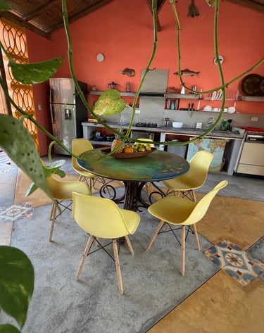 Rustic open-air kitchen with yellow mid-century chairs, a round table, and coral walls.