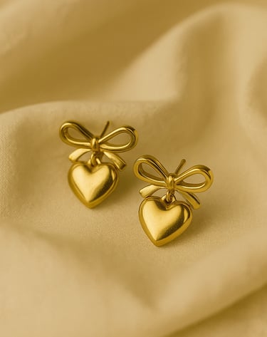 a pair of gold toned heart shaped earrings with a bow