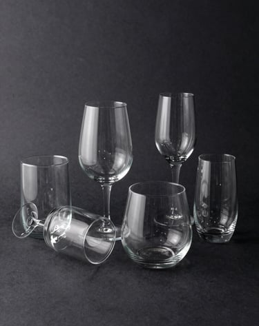 Creative composition of sleek glassware arranged on a deep charcoal black surface, featuring sharp reflections and high-end commercial lighting in a Central European studio.