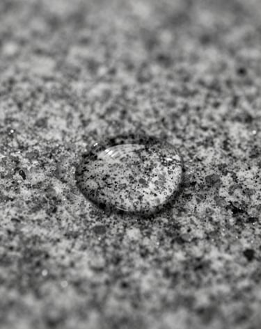 A black and white macro photograph of a drop of water on a textured granite surface, symbolizing the theme of water conservation with sharp focus and cinematic lighting.