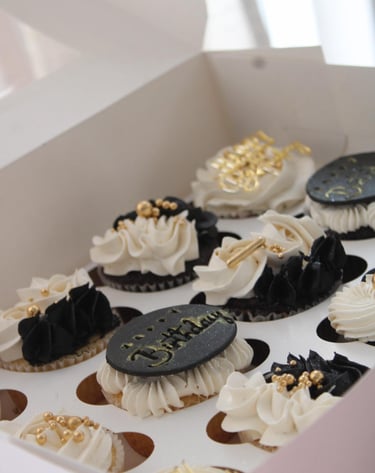 a box of cupcakes with white frosting and gold decorations