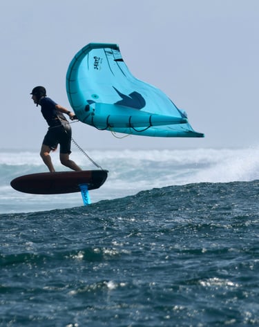 a man is holding a wing on a  foil board in the water, over a wave