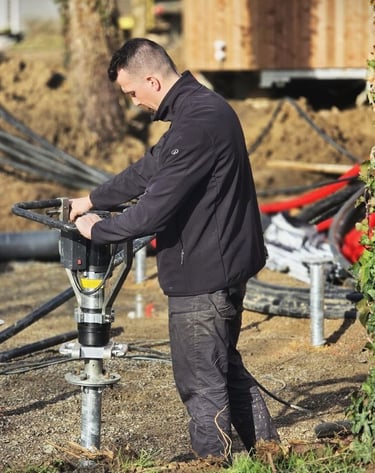 A construction worker installing a screw pile foundation for a new building using a handheld hydraulic drive.