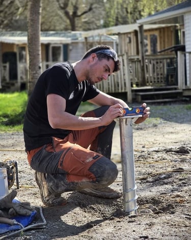 A worker using a spirit level to check the alignment of a ground screw foundation pile for a construction project.