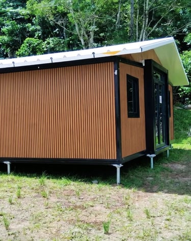 Modern wooden prefab tiny home on stilts located in a lush tropical forest clearing.