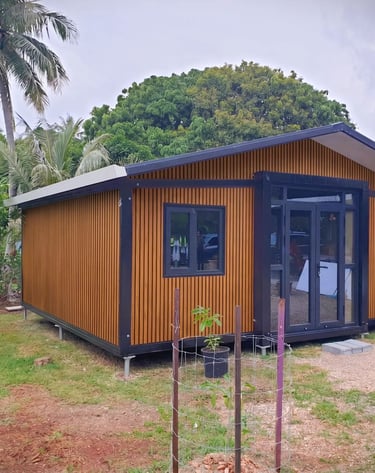 Modern wood-paneled tiny home or modular cabin with black trim nestled in a tropical landscape.